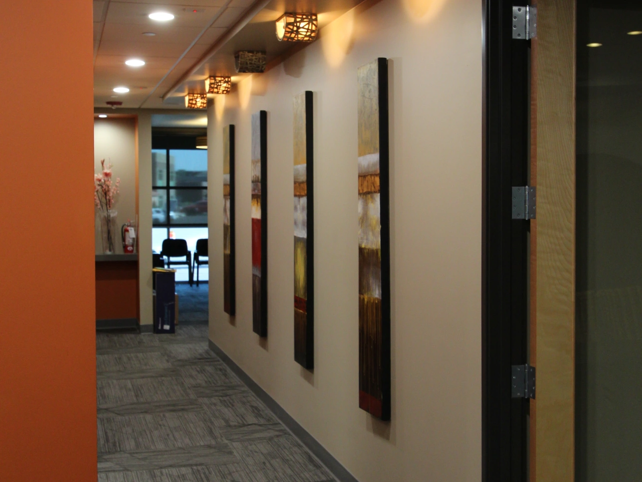Dental Office Hallway with Abstract Wall Art Panels, Decorative Ceiling Lights, and Waiting Area Visible in the Background