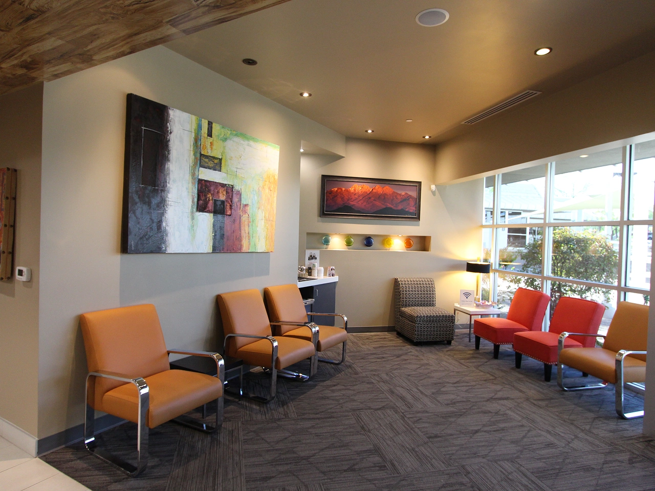 Bright Dental Office Waiting Room with Orange and Red Modern Chairs, Abstract Wall Art, and Large Windows